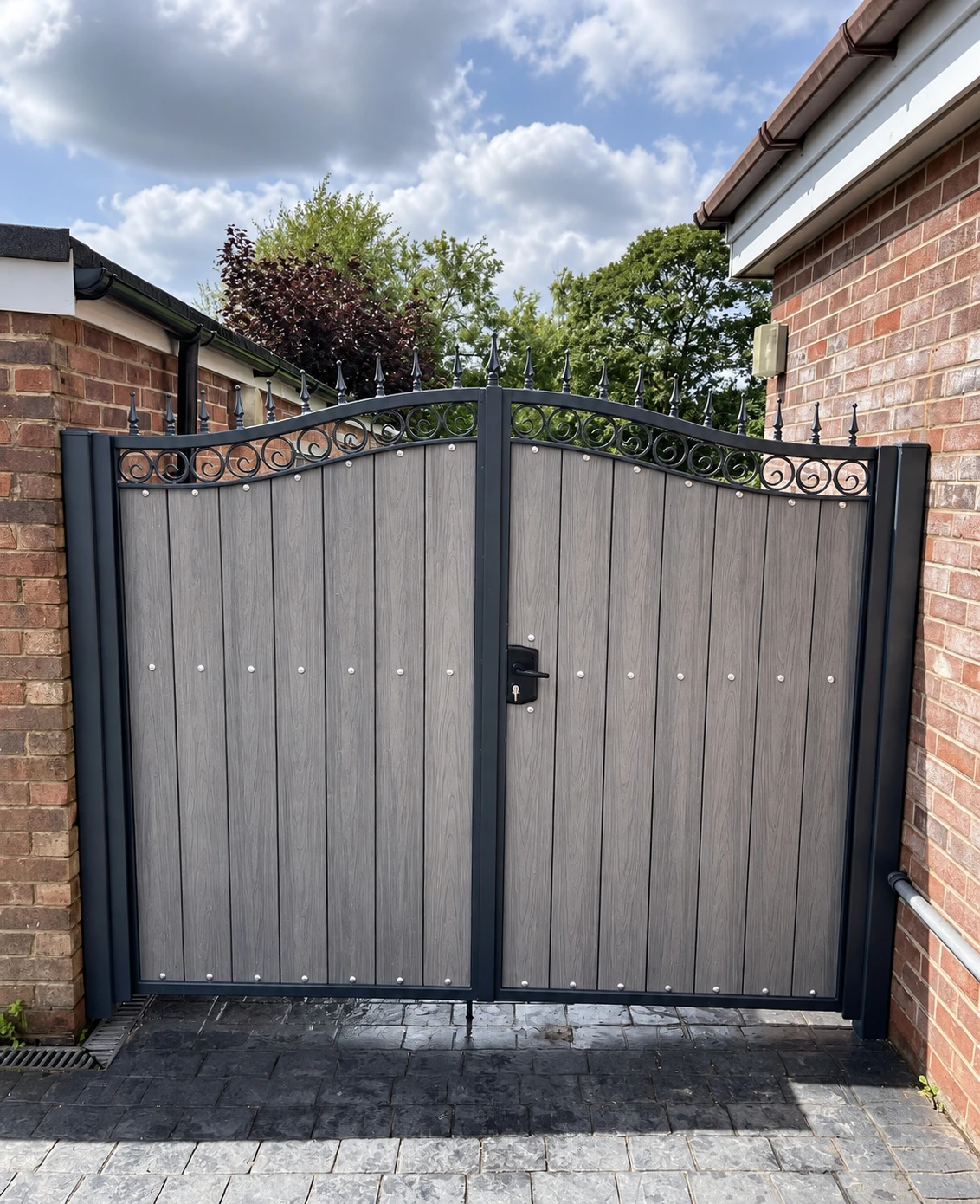Grey composite-look garden gate with a curved black metal top between brick walls