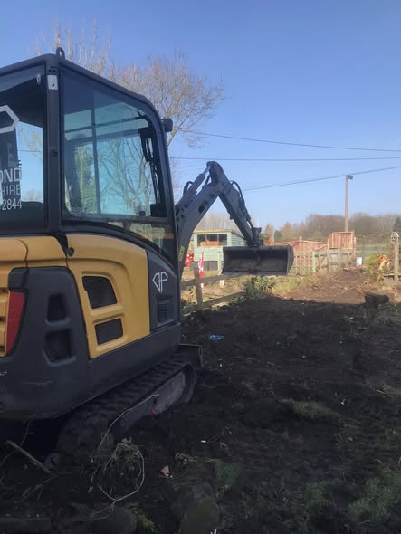 Cheddleton hedge-removal project with a yellow mini excavator working beside dark soil